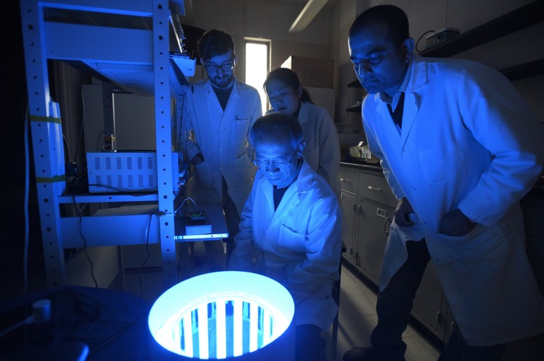 Zhuo-Hua Pan, with three laboratory members, look into a device emitting blue light in a dark lab