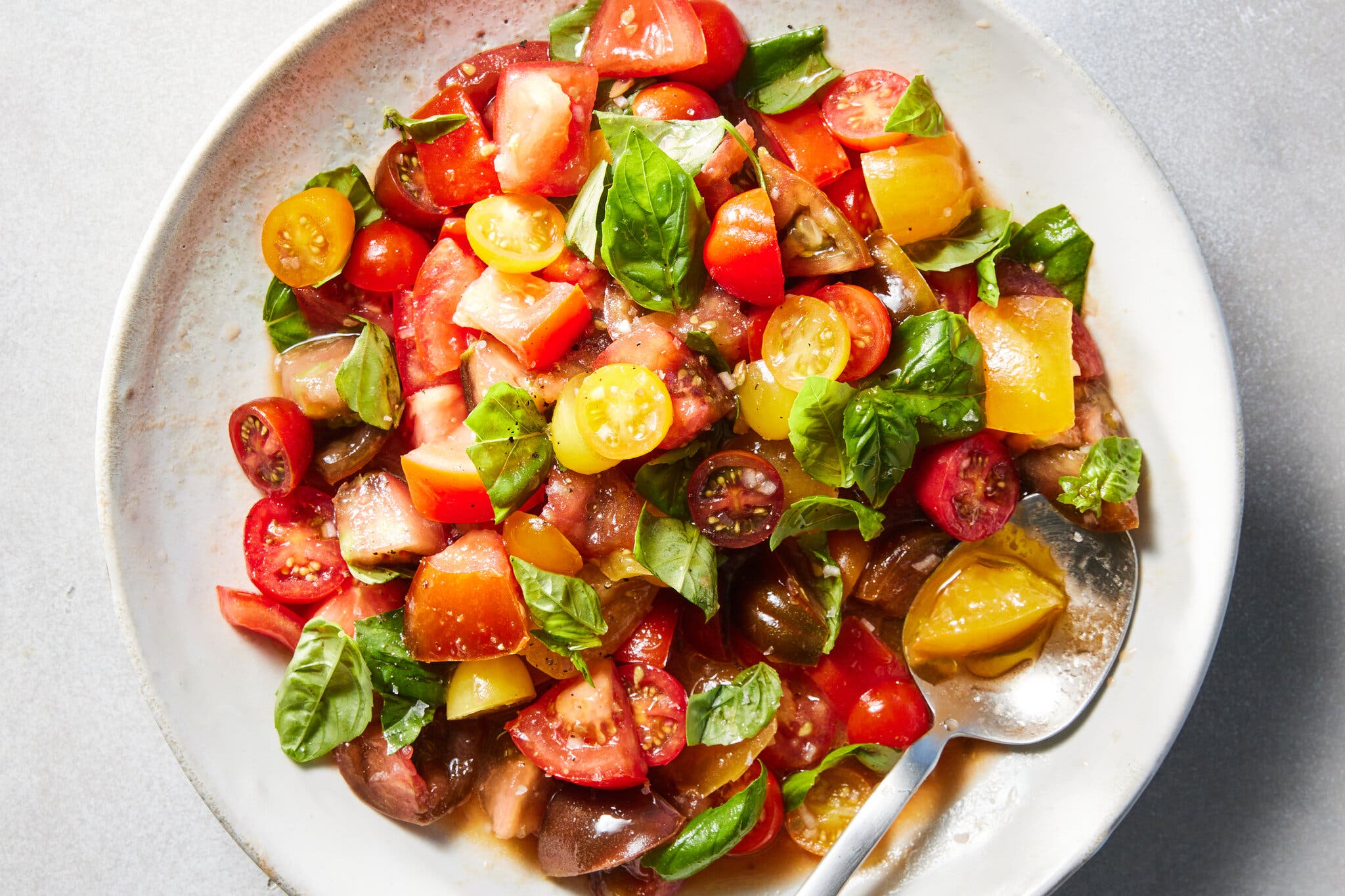 Halved cherry tomatoes sit in a bowl topped with basil. 