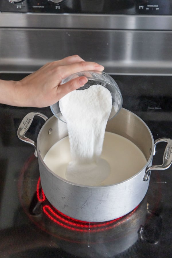 Pouring sugar mixture into a saucepan along with milk, cream, and glucose syrup.