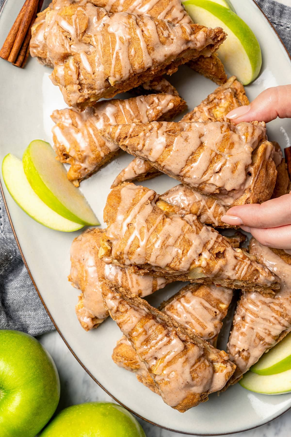 Hand grabbing glazed apple scone from platter