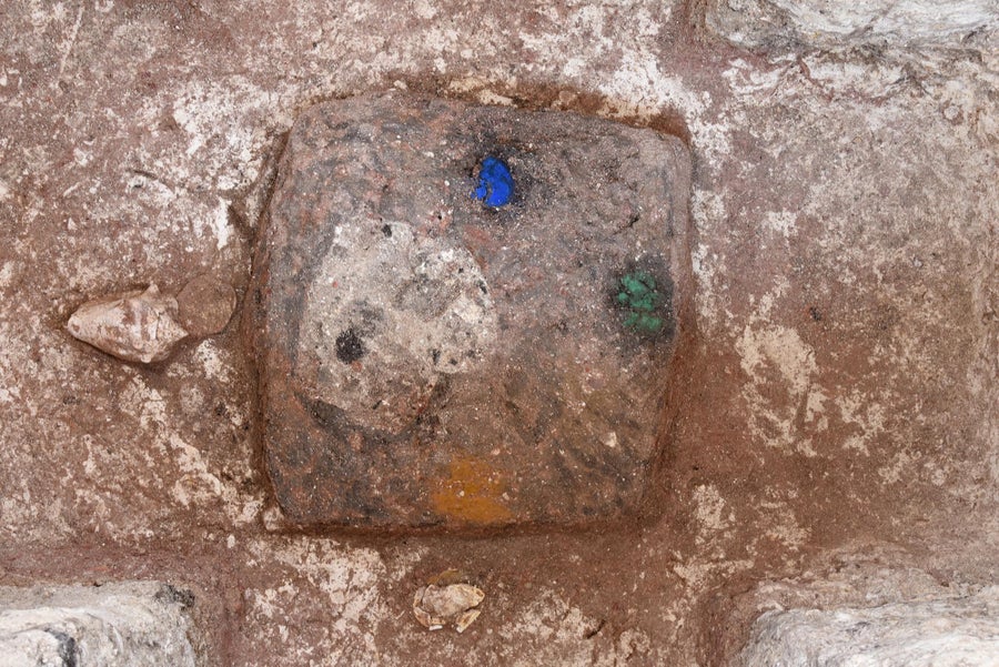 A stone square with a patch of blue to the top, green to the right, yellow at the bottom and cream-colored shell to the left