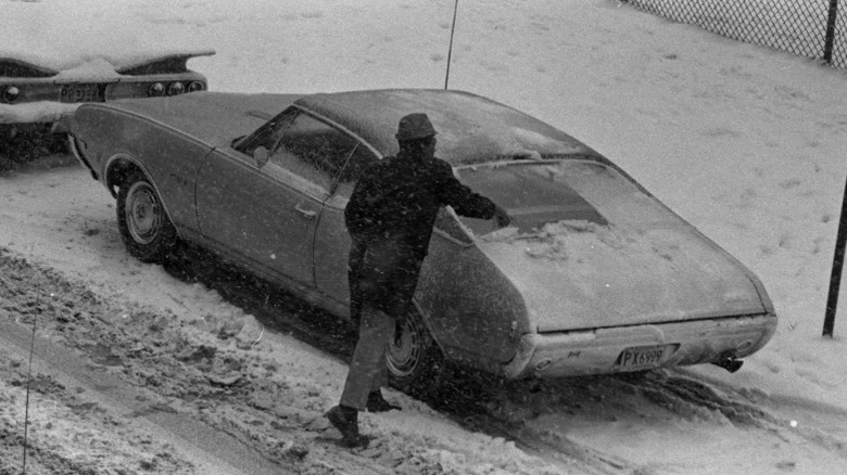 a black and white image of a person clearing snow off of the rear window of their car