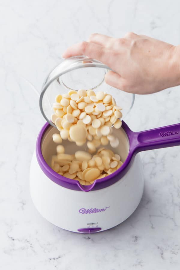 Pouring white chocolate callets into a chocolate melting pot.
