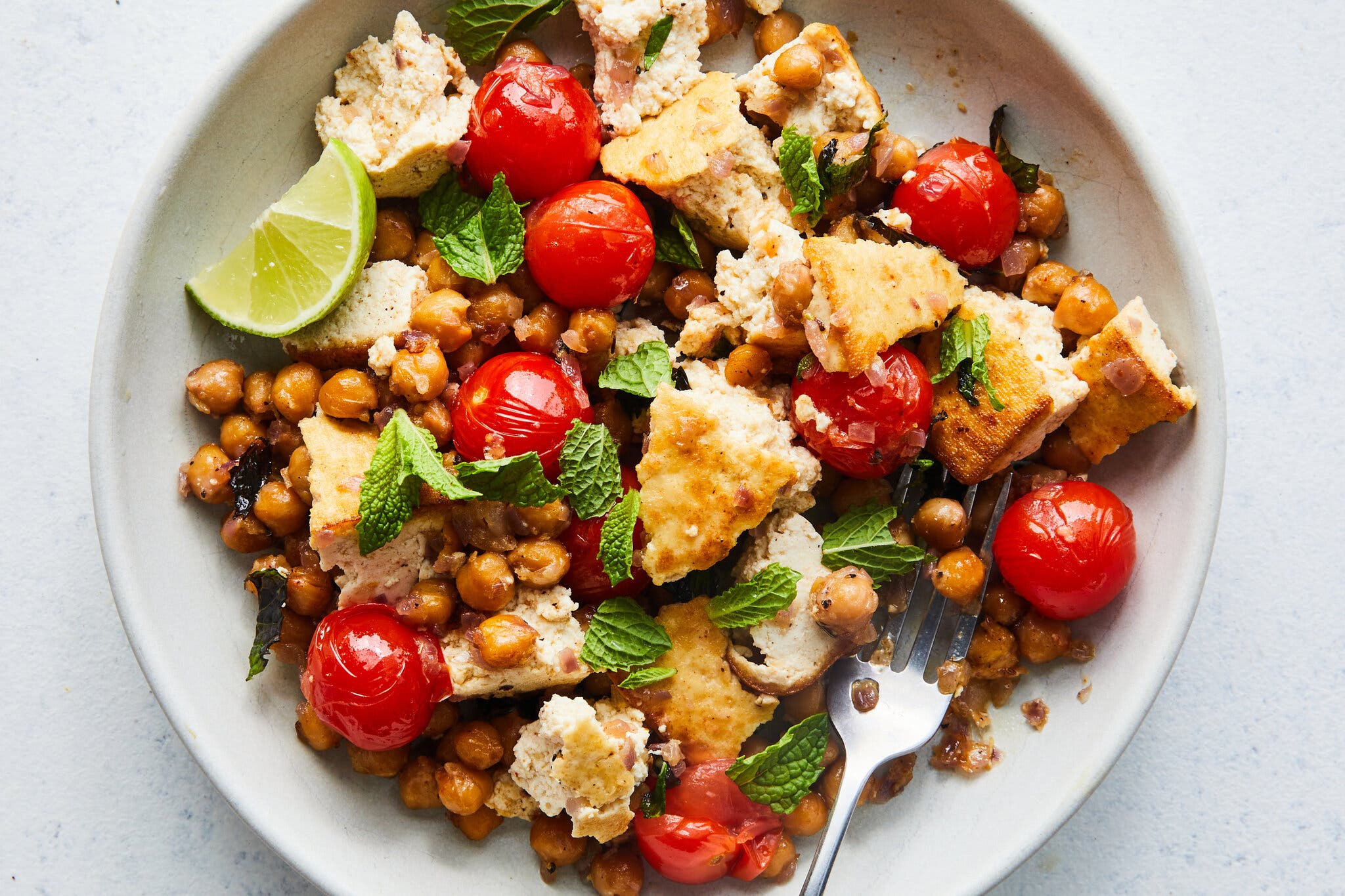 An overhead image of a plate topped with chickpeas, torn tofu, tomatoes and herbs.