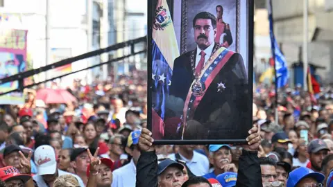 Getty Images A supporter of ousted Venezuela's President Nicolás Maduro carrieshis portrait during a rally outside the National Assembly in Caracas on Monday. Hundreds of people can be seen in the crowd. In the portrait of Maduro he is wearing a black suit, red tie and a sash bearing the colours of the Venezuelan flag. 