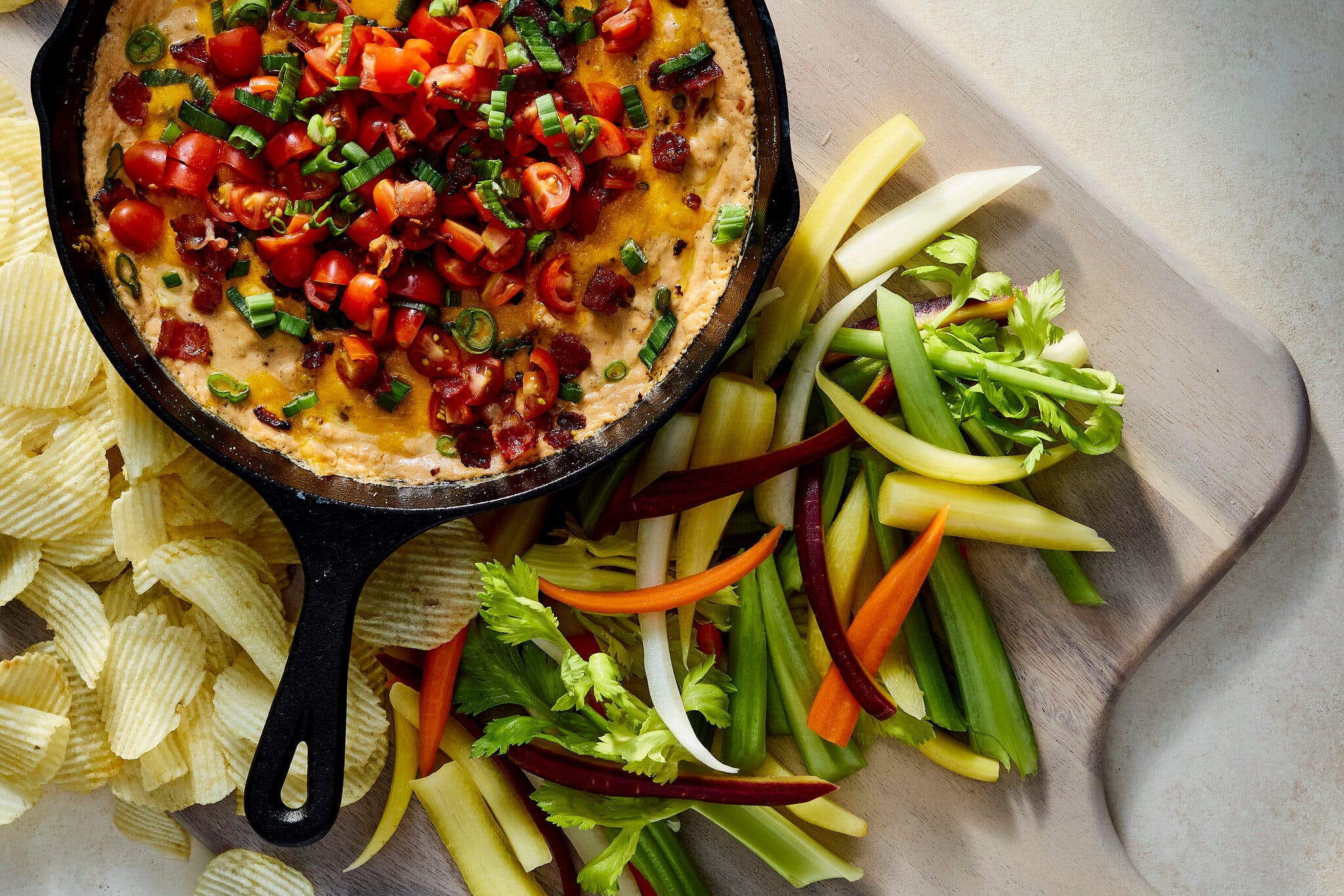 An overhead image of a hot dip in a cast-iron skillet surrounded by chips and vegetables for dipping.